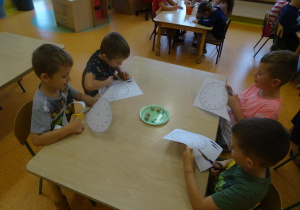 Czterech chłopców siedzi przy stoliku z nożyczkami w ręku, wycinają tarcze zegarów z papieru.